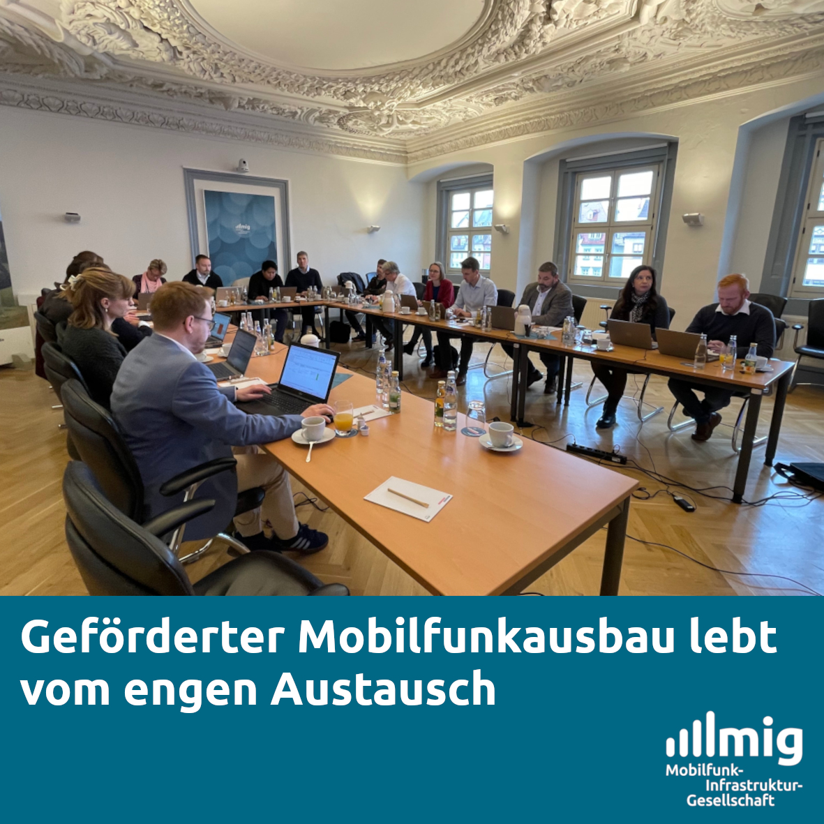 Das Foto einer Besprechung, bei dem die Teilnehmenden an einem u-förmig angeordneten Tisch sitzen. Im unteren Drittel eine blaue Fläche mit der Überschrift des Artikels und dem Logo der MIG.