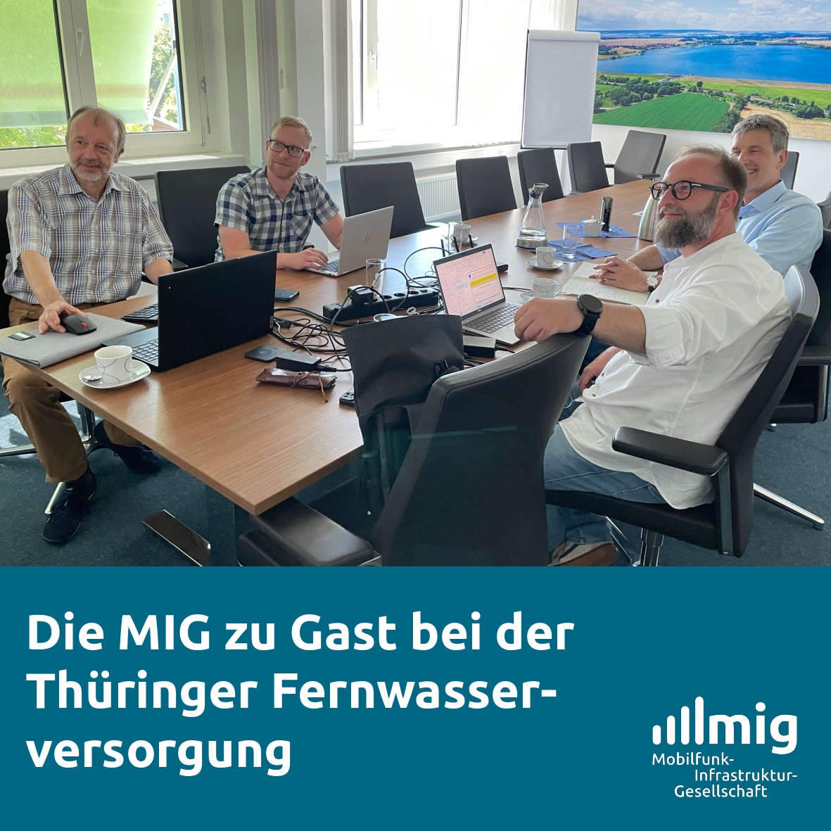 Vier Männer sitzen an einem Konferenztisch und schauen auf eine nicht im Bild sichtbare Präsentation an der Wand.